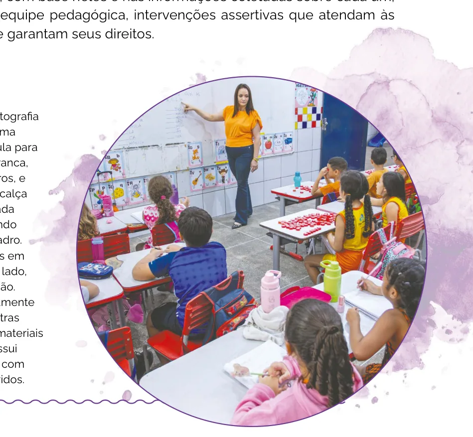 Fotografia de uma professora ministrando aula para uma turma de crianças sentadas em suas mesas, apontando para o quadro